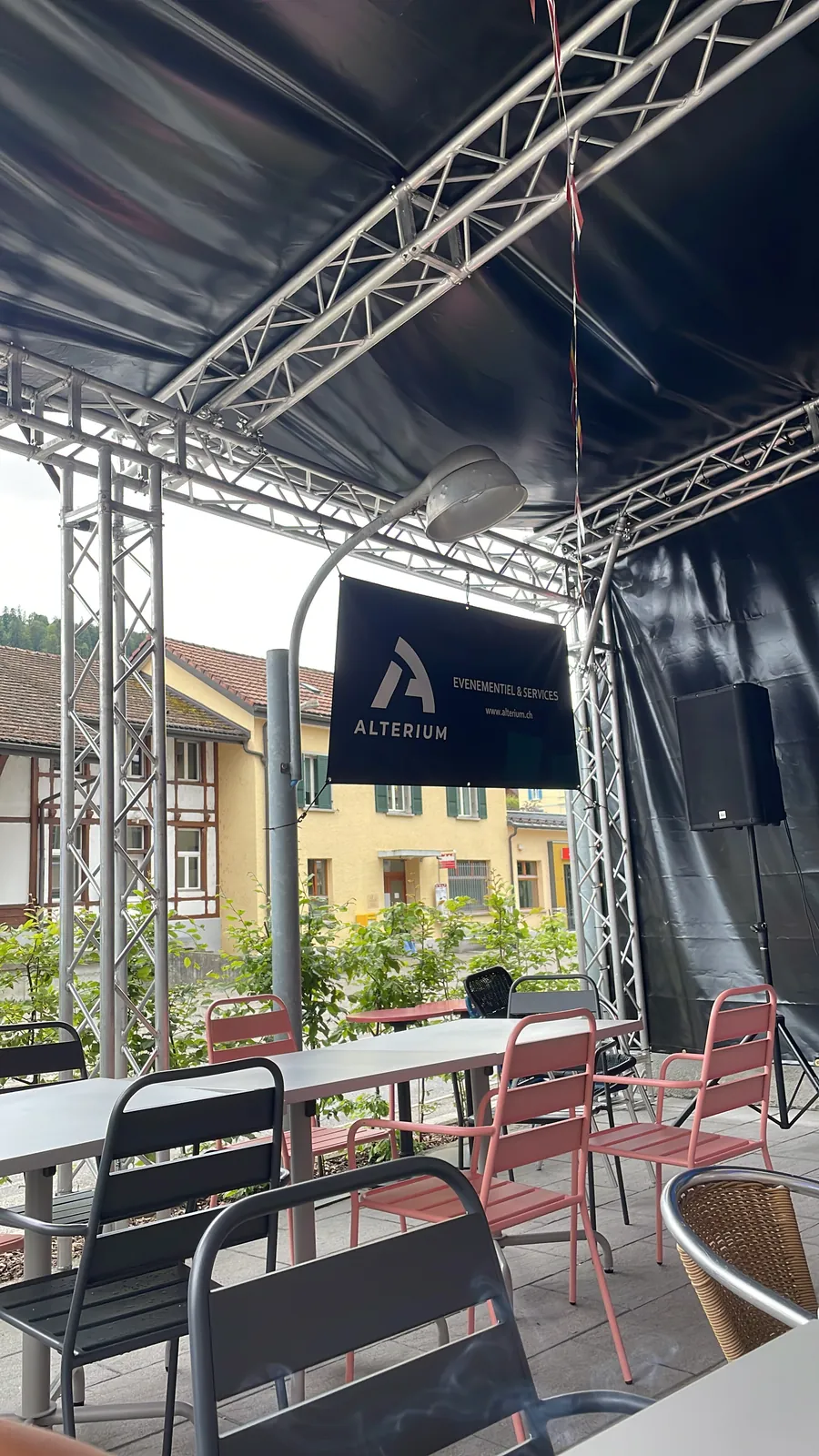 Sous le couvert de la fan zone en 2024 : tables et chaises de la terrasse, structure truss, enceinte sur pied et bâche Alterium suspendue