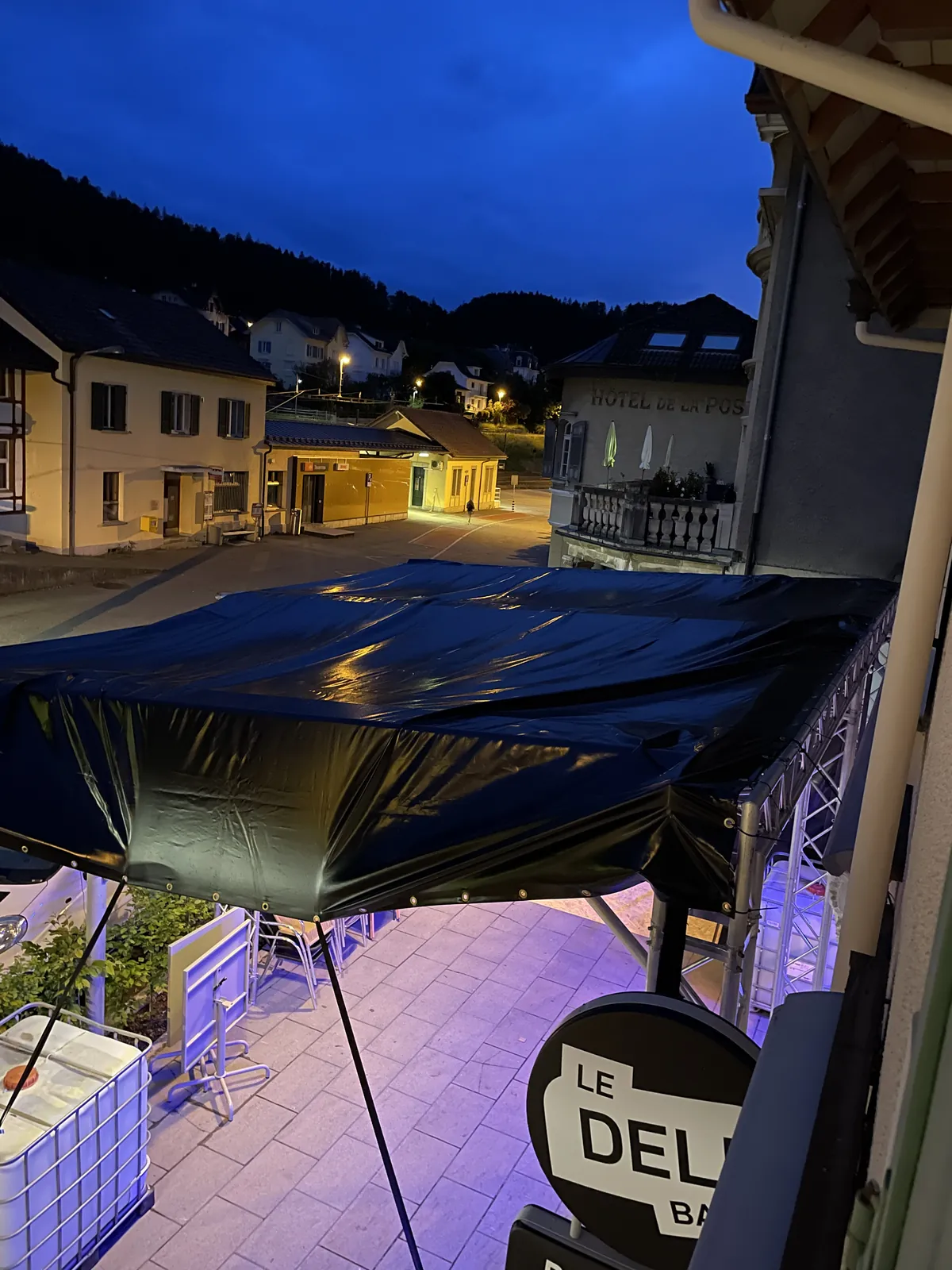 Le couvert de la fan zone vu d'en haut à la tombée de la nuit, terrasse éclairée en violet et enseigne du Deli Bar au premier plan, en 2024